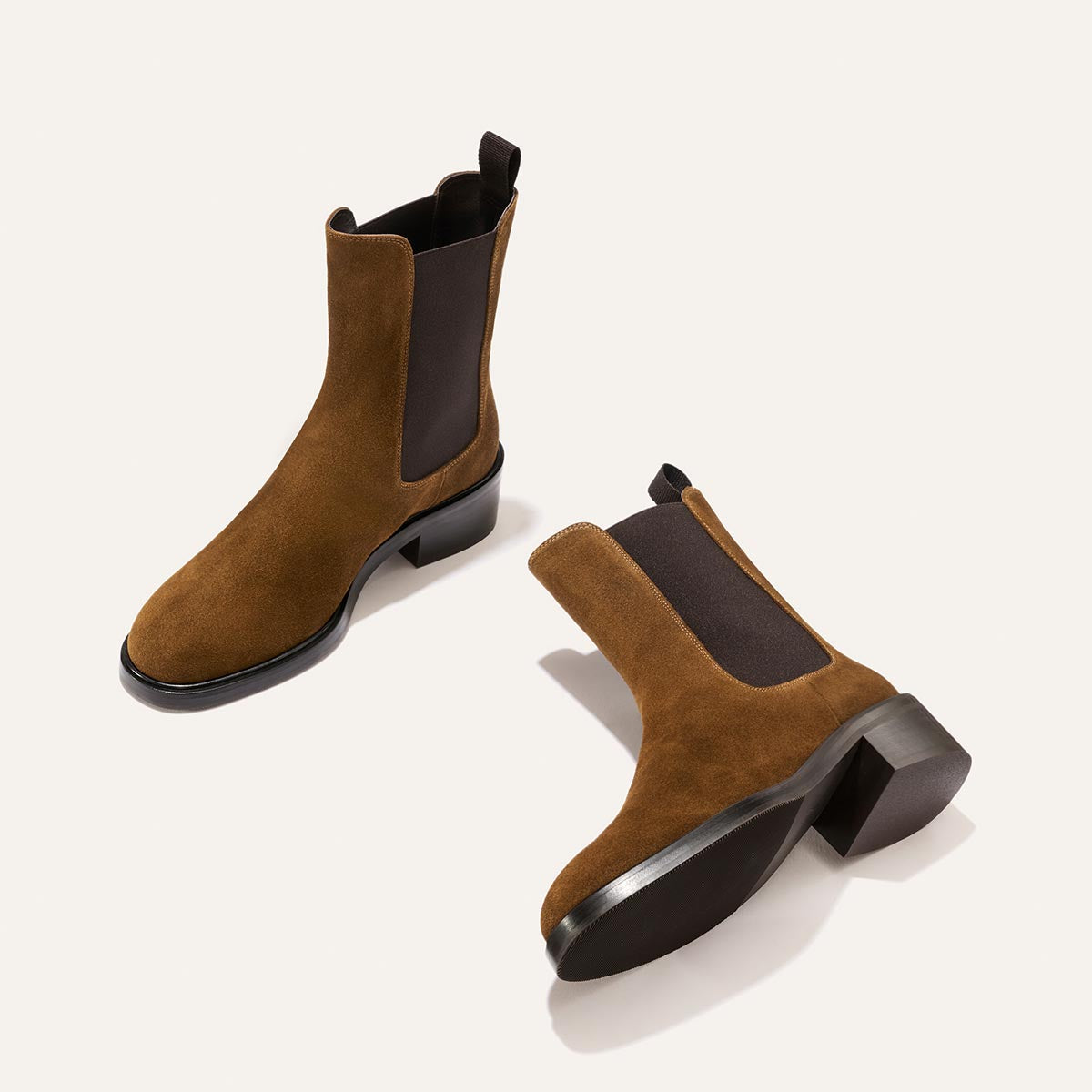 A pair of The City Chelsea Boot - Cedar Suede by Margaux, featuring brown suede with black elastic side panels and black heels, positioned on a light background.