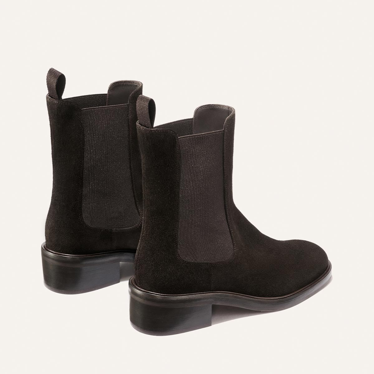 A pair of Margaux’s The City Chelsea Boot in dark chocolate suede, featuring elastic side panels and pull tabs, displayed from the back and side angles against a plain light background.