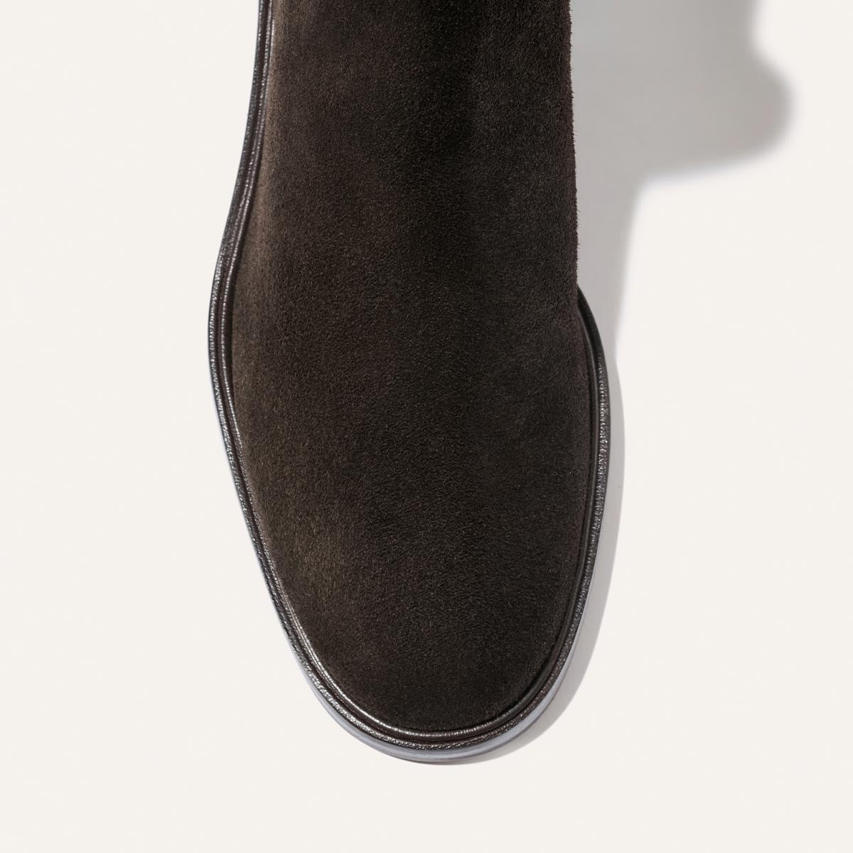 A close-up, top-down view of the toe and upper section of Margaux’s The City Chelsea Boot in Dark Chocolate Suede, featuring a rounded square shape and a visible black edge, displayed on a white background.