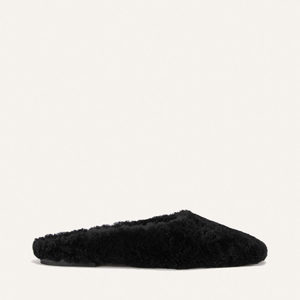 The Clara - Black Shearling slipper by Margaux is displayed in a side view against a plain white background, showcasing its cozy, slip-on silhouette and stylish black shearling finish.