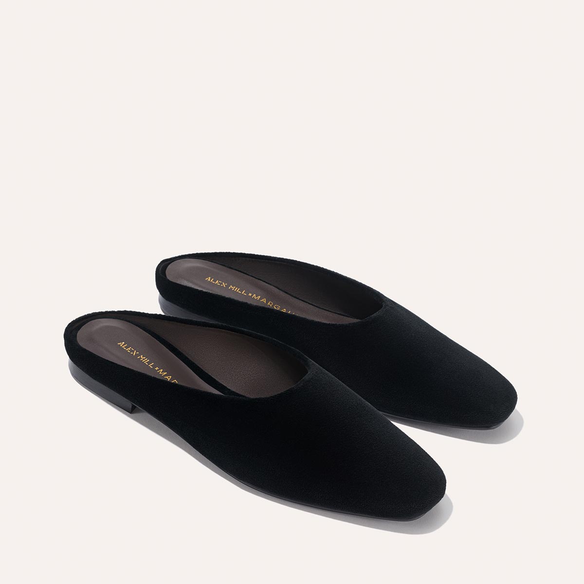The Clara – Black Velvet by Margaux: black velvet slip-on mules with low heels, gold branding inside, shown on a light background. A stylishly versatile design from the Alex Mill x Margaux collaboration.