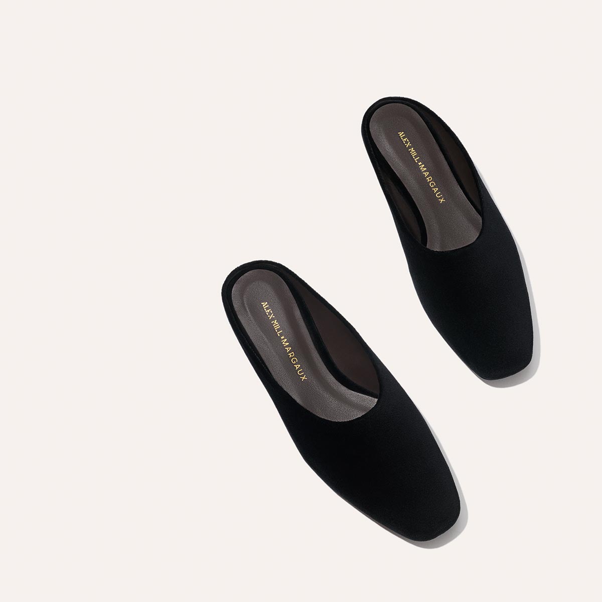A pair of black velvet slip-on mules, “Alex Mill x Margaux: The Clara - Black Velvet” by Margaux, featuring a square toe and flat sole, displayed on a light background—versatile style for any look.