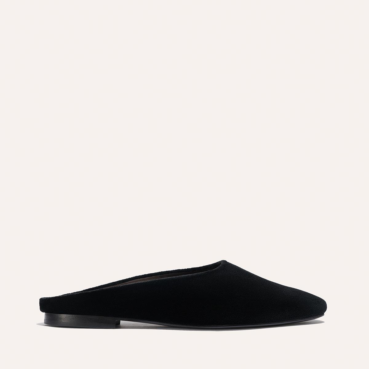 The Alex Mill x Margaux: The Clara - Black Velvet by Margaux is a single black velvet slip-on mule with a closed toe and flat sole, shown in profile on a light background, highlighting its stylish versatility.