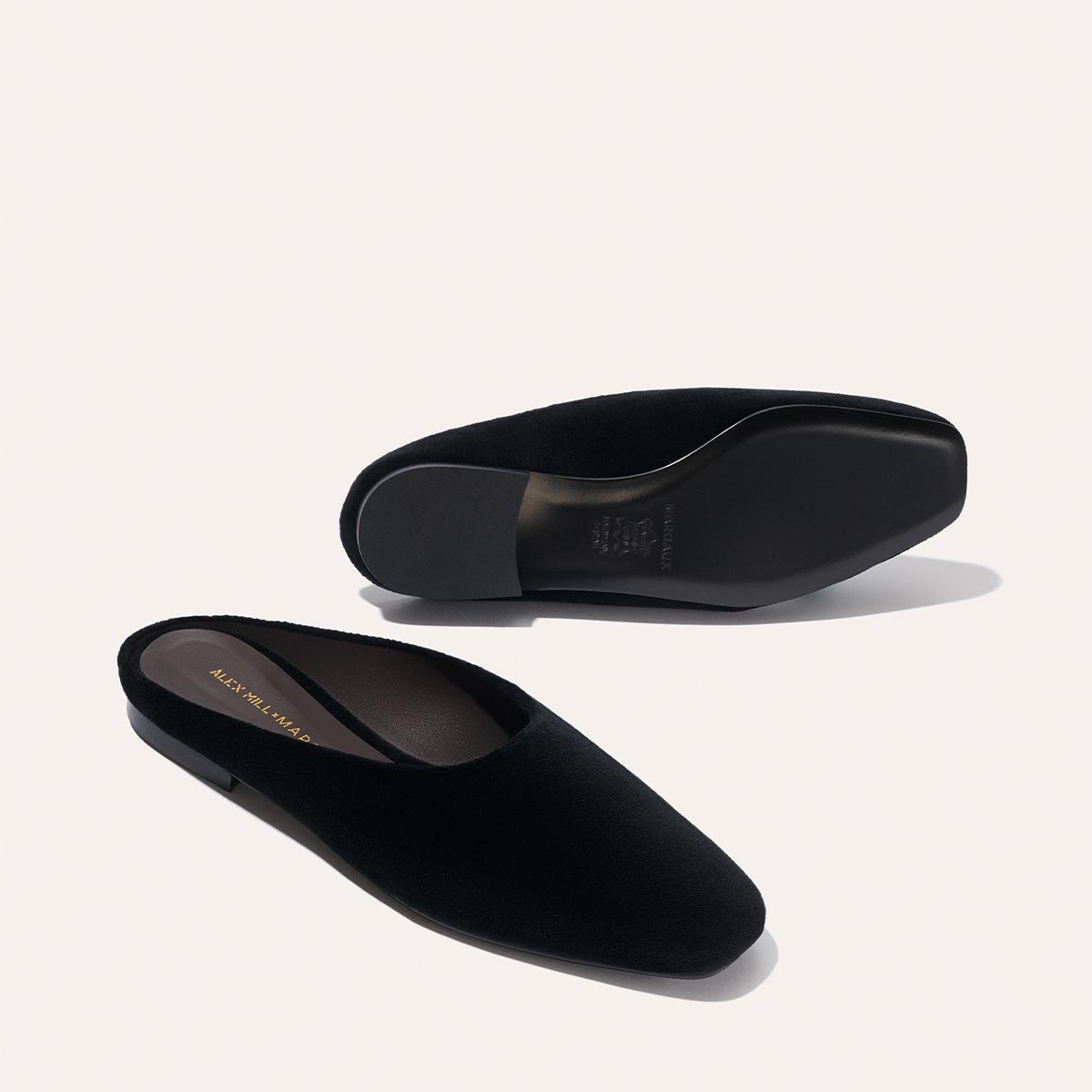 Margaux’s Alex Mill x Margaux: The Clara - Black Velvet slip-on mules feature square toes and a smooth sole, displayed one upright and one sole-up on a light background, highlighting their stylish versatility.