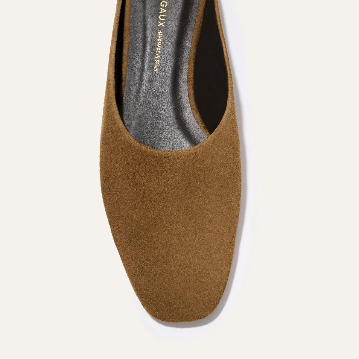 A close-up top view of Margaux's The Clara - Cedar Suede flat, featuring brown suede, a square toe, and a black cushioned insole, set against a light background.
