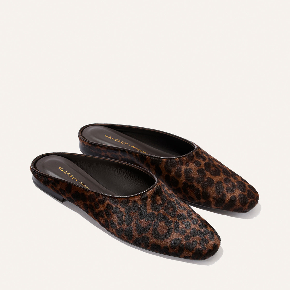 Introducing The Clara - Chocolate Leopard Haircalf by Margaux: a pair of flat slip-on mule shoes featuring a striking brown and black leopard print pattern, comfortable flat soles, and sleek black interiors. Displayed on a light background, these versatile slippers are the perfect choice for anyone looking to combine all-day comfort with standout style.