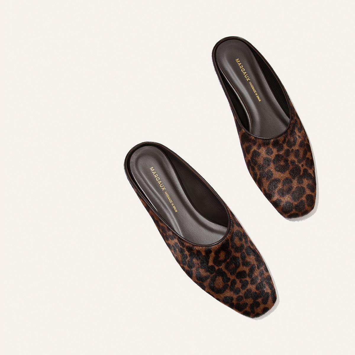 A pair of The Clara slip-on shoes by Margaux in Chocolate Leopard Haircalf are displayed on a light background.