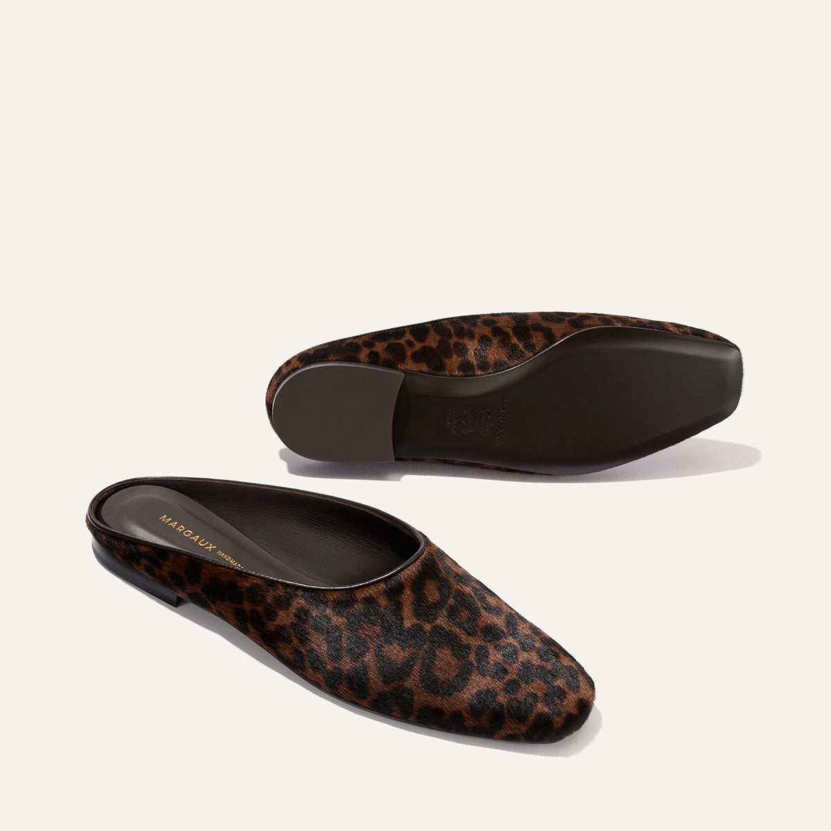 A pair of Margaux’s “The Clara” loafers in Chocolate Leopard Haircalf—one laid flat and the other on its side to reveal the dark sole and branded insole—offers a versatile, backless silhouette that blends do-it-all style with slipper-like comfort.