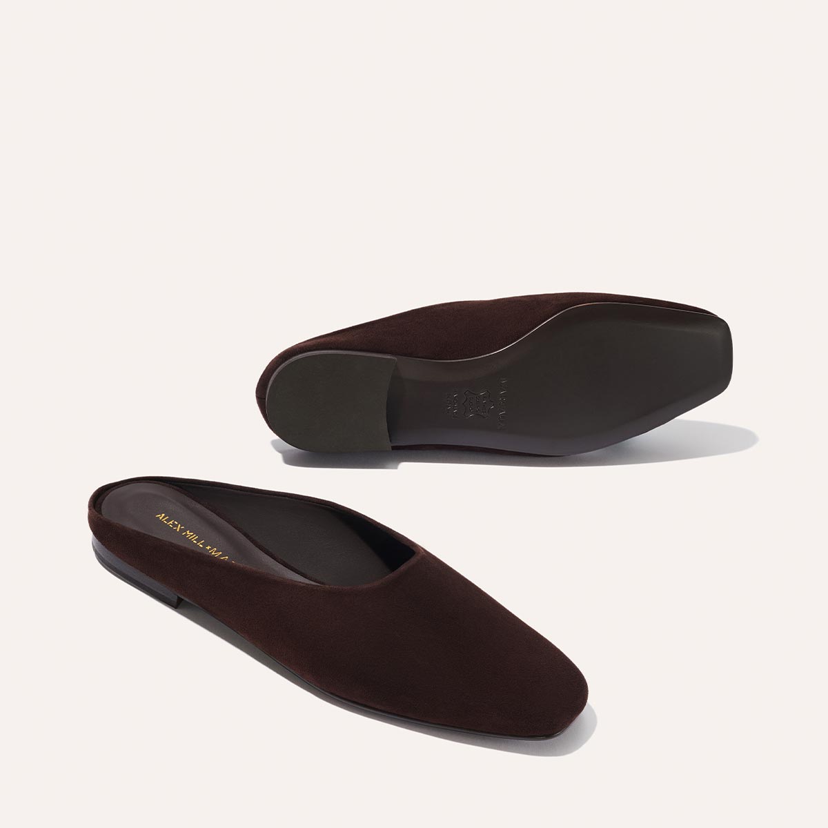 The Clara - Espresso Suede by Margaux: brown suede slip-on shoes with flat soles and a slipper-like shape, shown on a light background. One shoe stands upright, the other displays its sole.