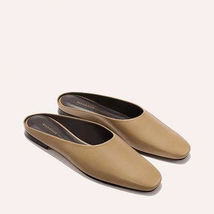The Clara - Praline Calf by Margaux: tan leather slip-on mules with a low, flat black heel and rounded square toe, shown on a light neutral background.