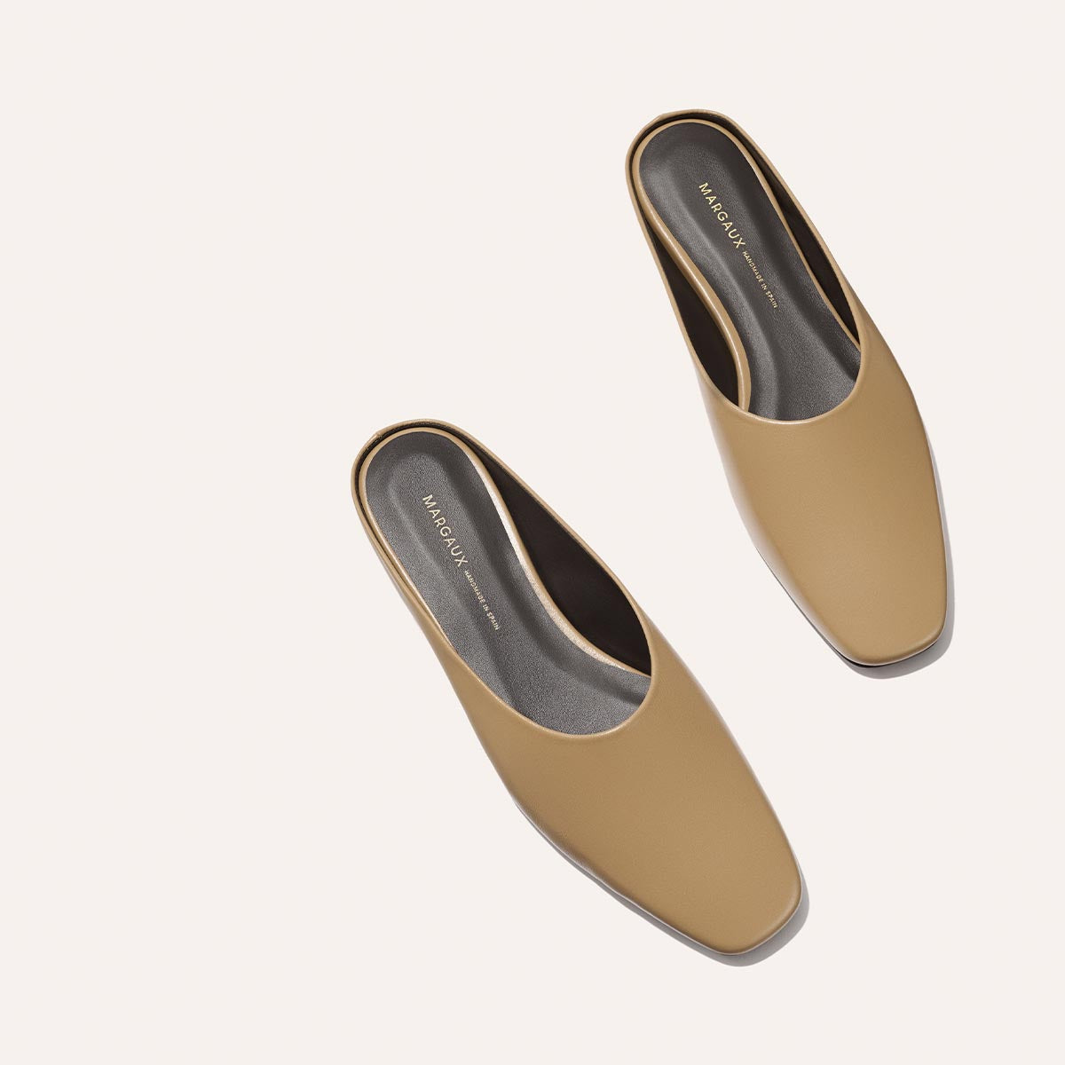 A pair of The Clara - Praline Calf slip-on mule shoes by Margaux with square toes, shown on a light background. The insoles are dark and feature Margaux branding on each shoe.