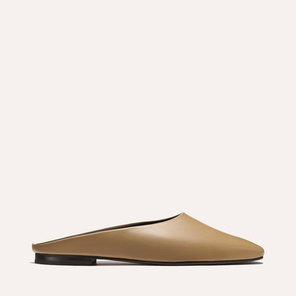The Clara - Praline Calf by Margaux is a tan slip-on mule with a closed toe and flat black sole, shown in profile against a plain, light background.