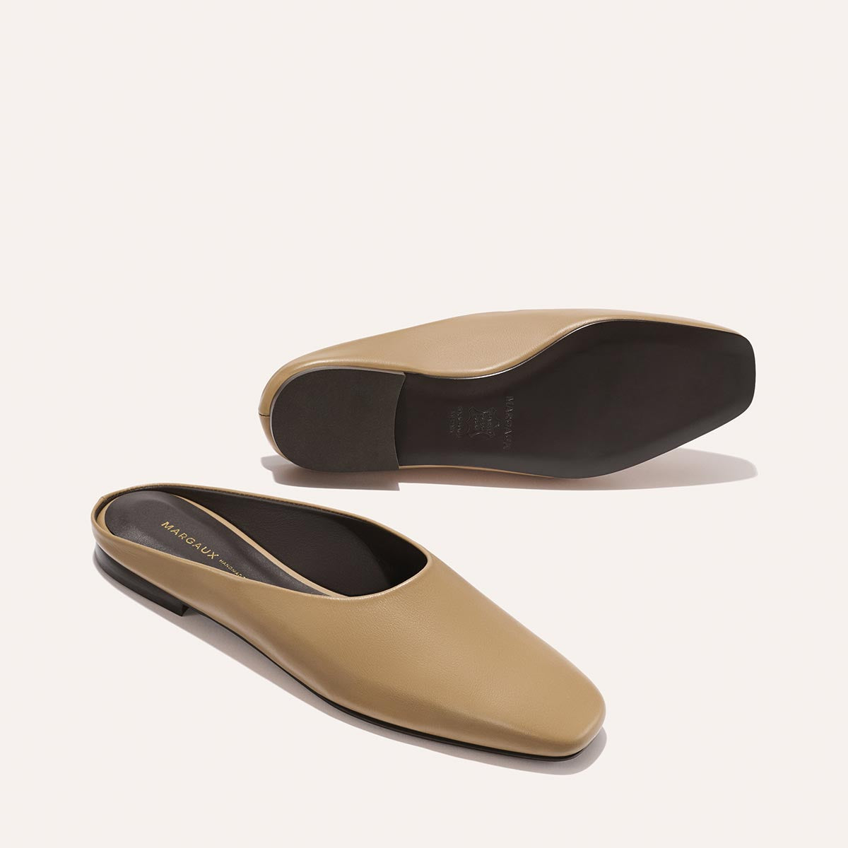 The Clara - Praline Calf by Margaux: Tan leather slip-on mules with a square toe and low heel, shown from the side and sole on a light background.