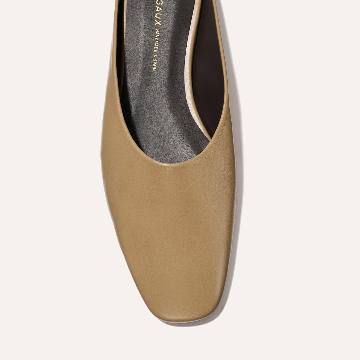A close-up overhead view of Margaux’s The Clara - Praline Calf, a tan square-toe flat with a black insole and minimal design, set against a light background.