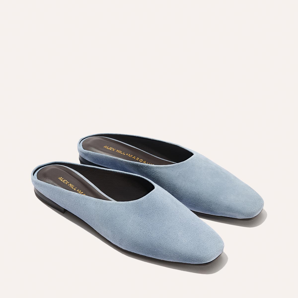 The Margaux Alex Mill x Margaux: The Clara - Slate Blue Suede mules feature almond-shaped toes, a low heel, black insole, and versatile slip-on design, shown on a neutral backdrop.