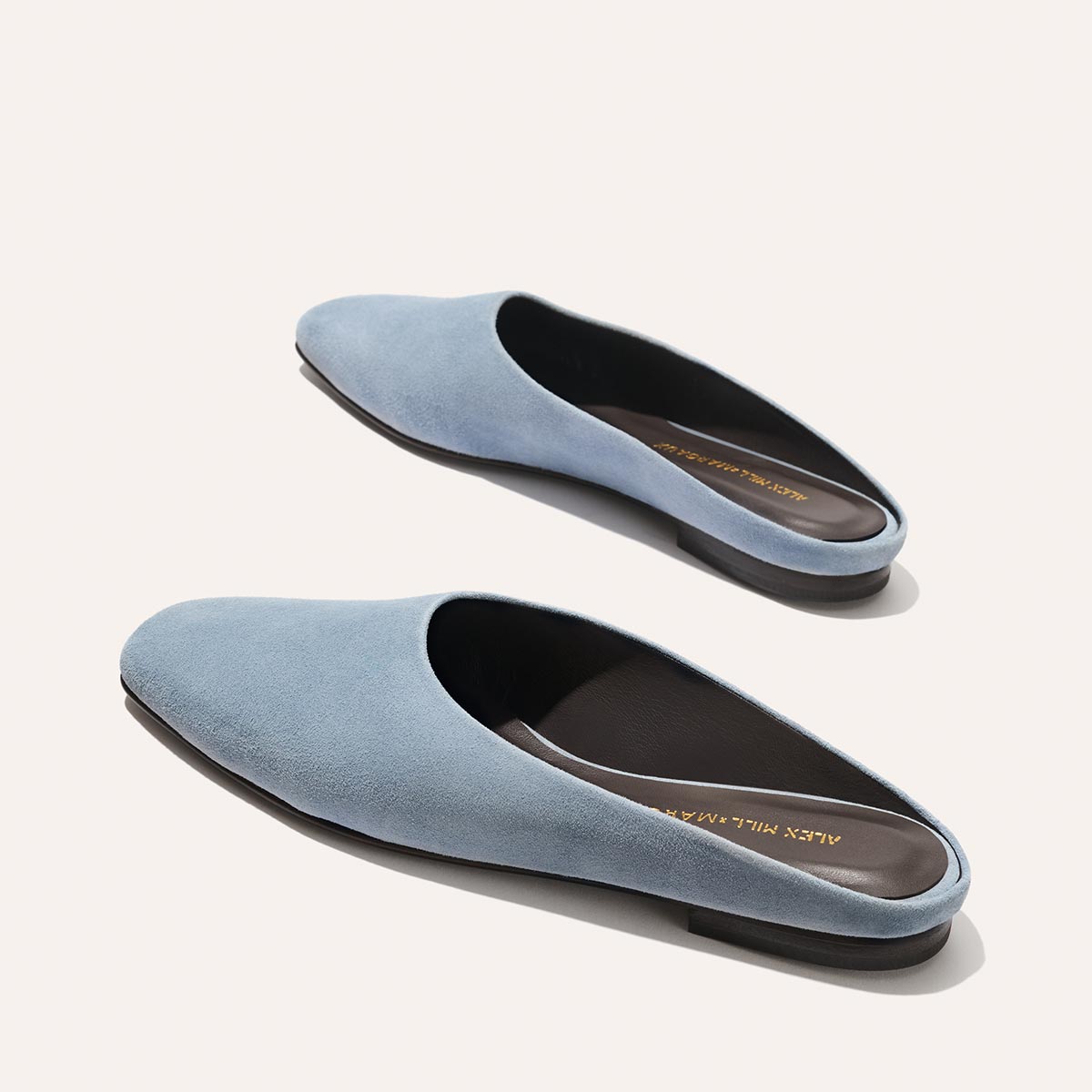 The Margaux Alex Mill x Margaux: The Clara - Slate Blue Suede features closed toes, brown insoles, and black soles—a stylish, versatile slip-on flat shown on a light background.