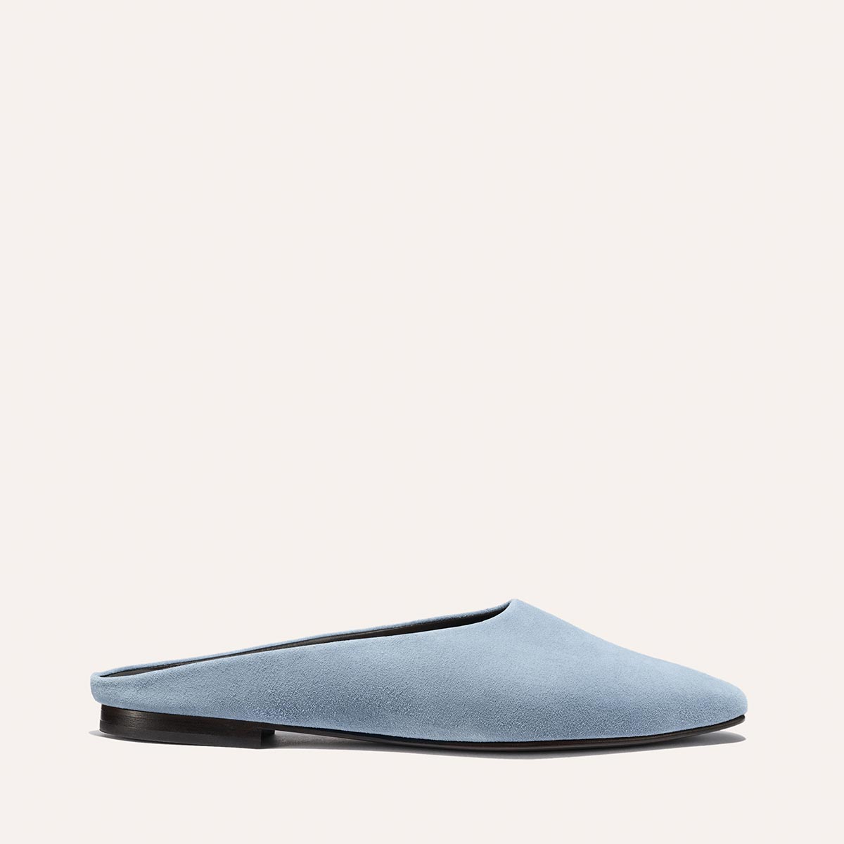 The Margaux Alex Mill x Margaux: The Clara - Slate Blue Suede features a light blue suede slip-on mule with a closed toe and flat black sole, offering versatile style against a plain, light background.