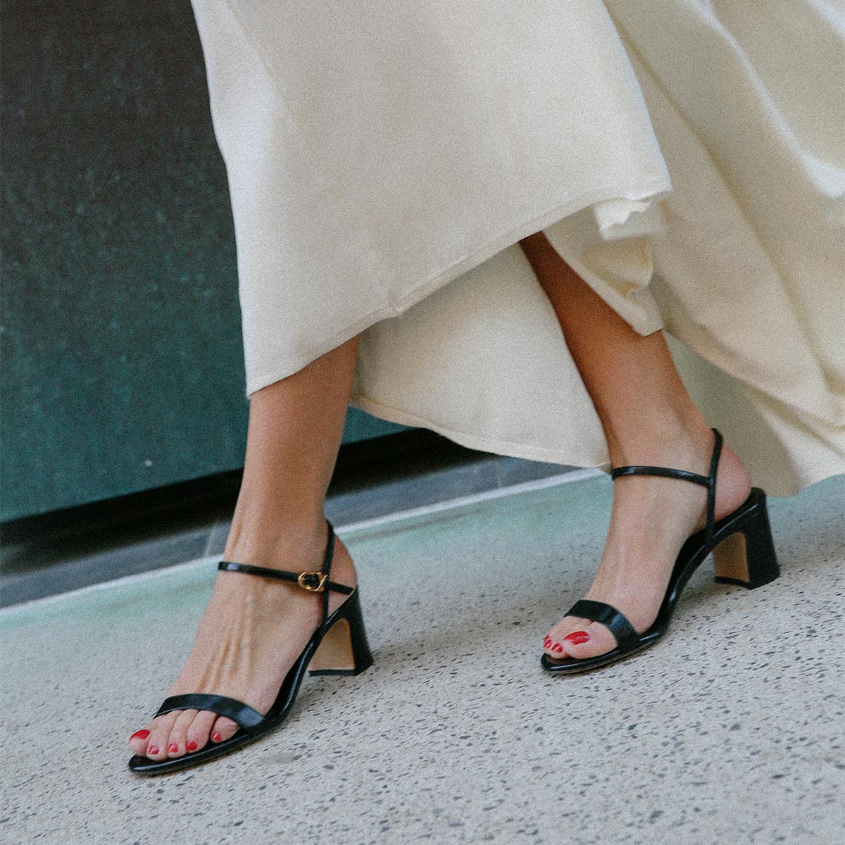 The Cleo Sandal in Black Crinkle-Gloss Nappa styled with a white dress.