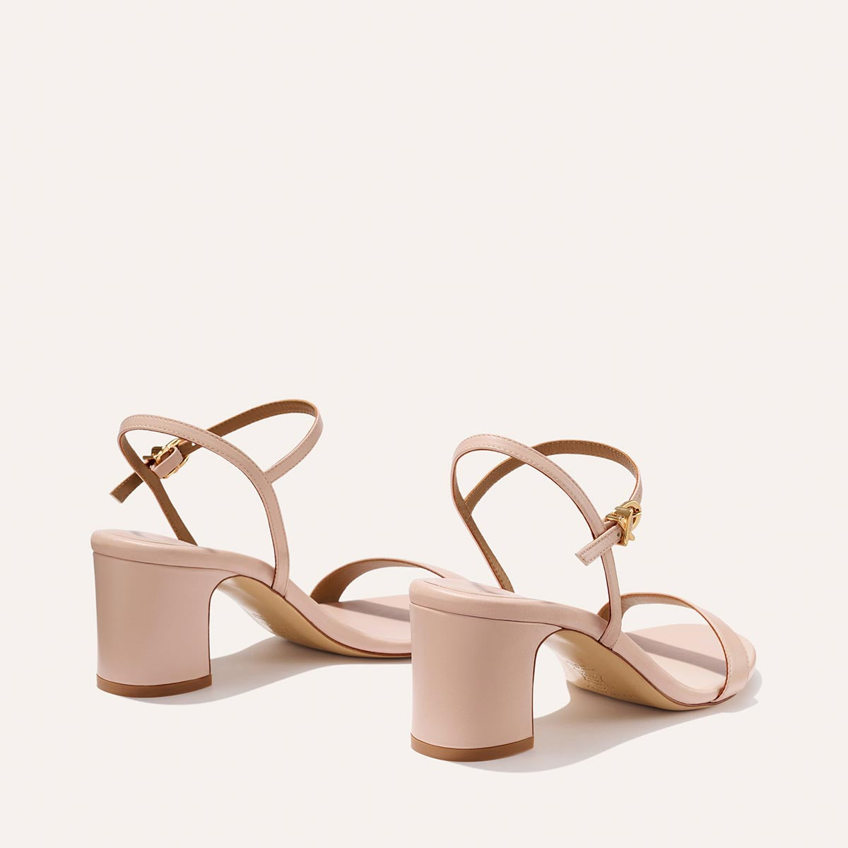 The Cleo Sandal - Petal Nappa by Margaux features light pink, open-toe design with mid-height comfortable heels and thin ankle straps with gold buckles, displayed on a plain light background.
