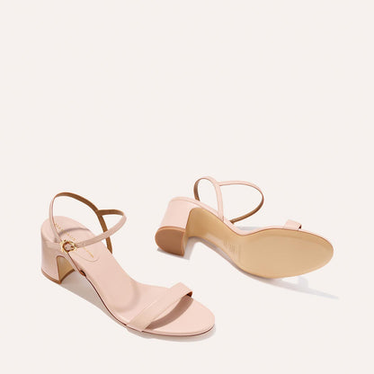 The Cleo Sandal - Petal Nappa by Margaux features light pink open-toe block heels with ankle straps and gold buckles, offering comfort and style, shown on a plain off-white background.