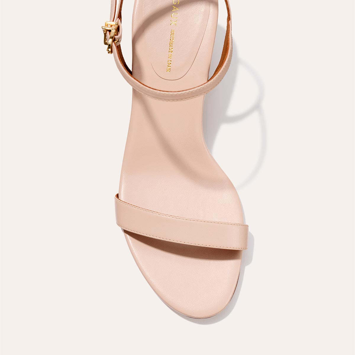 The Cleo Sandal - Petal Nappa by Margaux: a beige open-toe sandal with a single front strap, gold-buckled ankle strap, and flattering heel, shown from above on a light background.