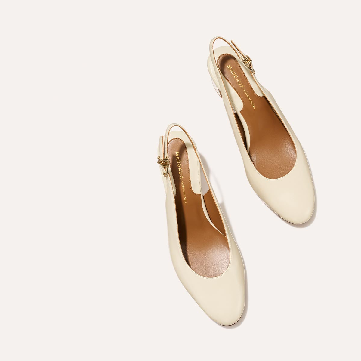 The Cluny Slingback in Cream Nappa, featuring a sleek Italian nappa leather upper with an adjustable buckle and a comfortable 2.5-inch black heel.