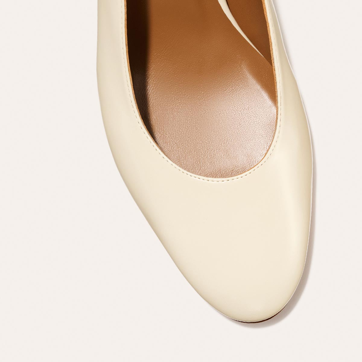 The Cluny Slingback in Cream Nappa, featuring a sleek Italian nappa leather upper with an adjustable buckle and a comfortable 2.5-inch black heel.