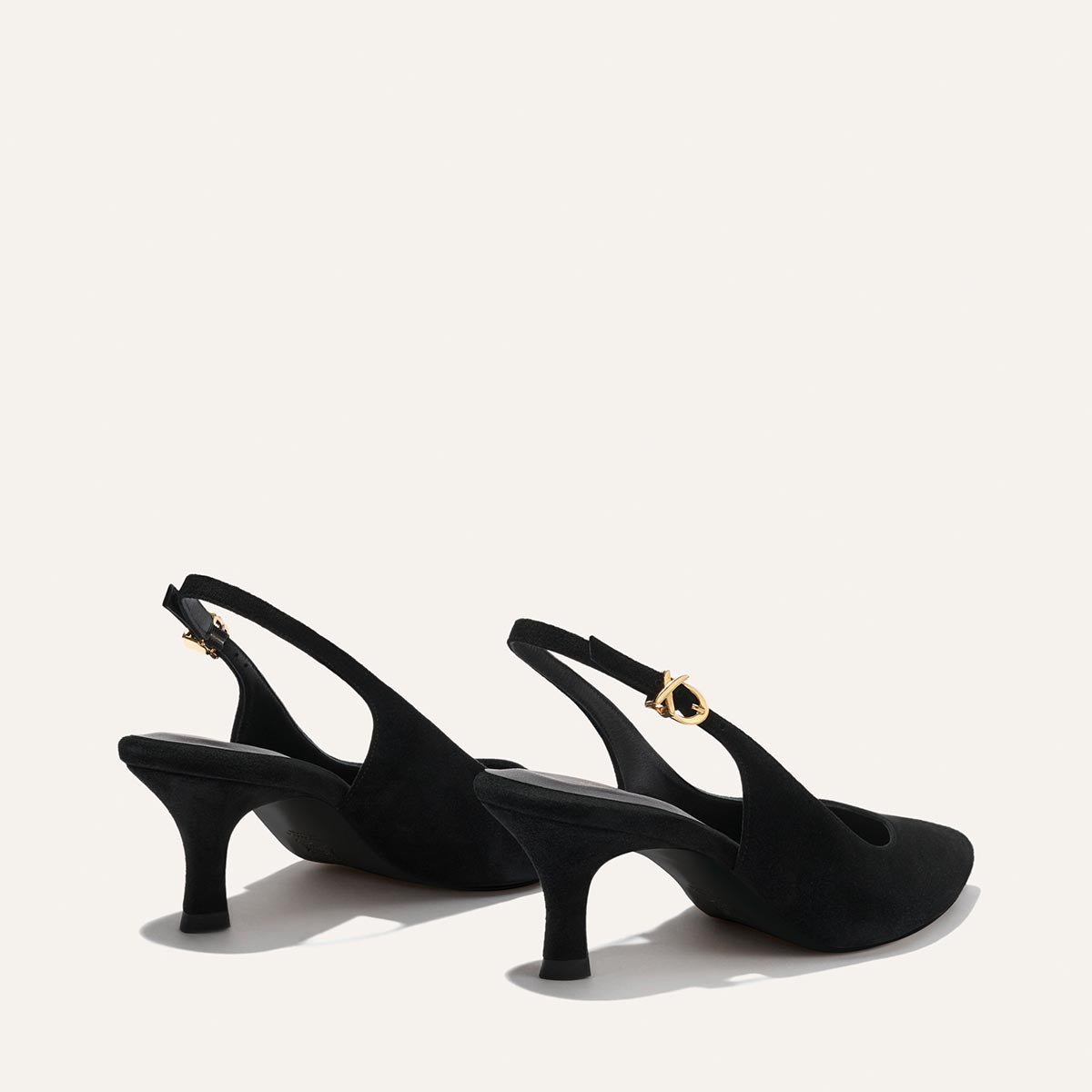 The Colette - Black Suede by Margaux: a pair of black suede slingback heels with mid-height curved heels and gold buckle closures, shown against a light background.