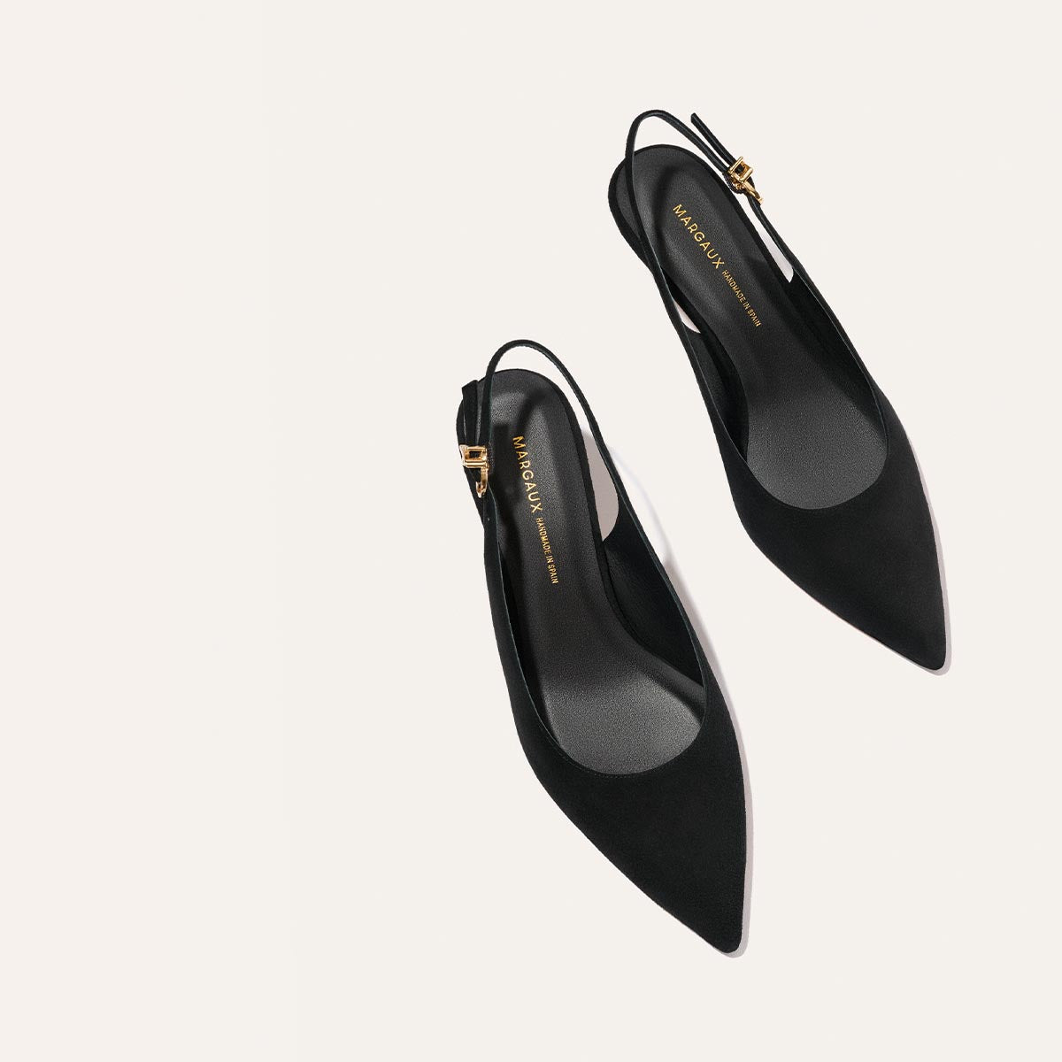 The Colette - Black Suede by Margaux: black pointed-toe slingback heels with gold buckle strap details, displayed on a light neutral background.