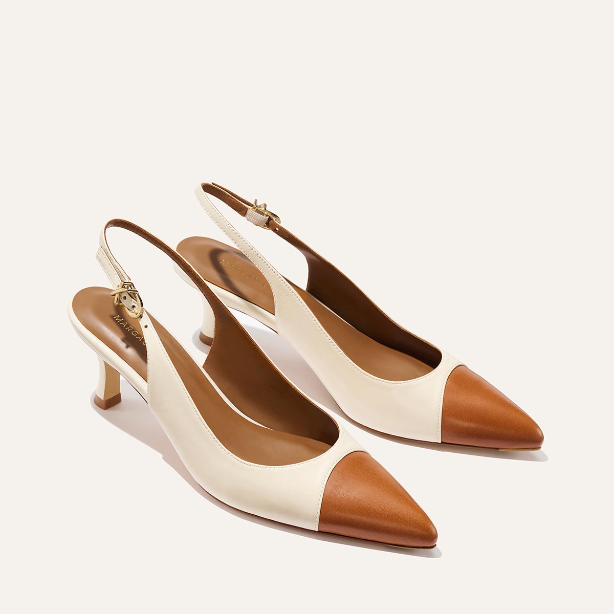 The Colette by Margaux is a pair of women's slingback heels in cream cotton and brown saddle nappa, featuring a micro heel and an adjustable ankle strap with a gold buckle.