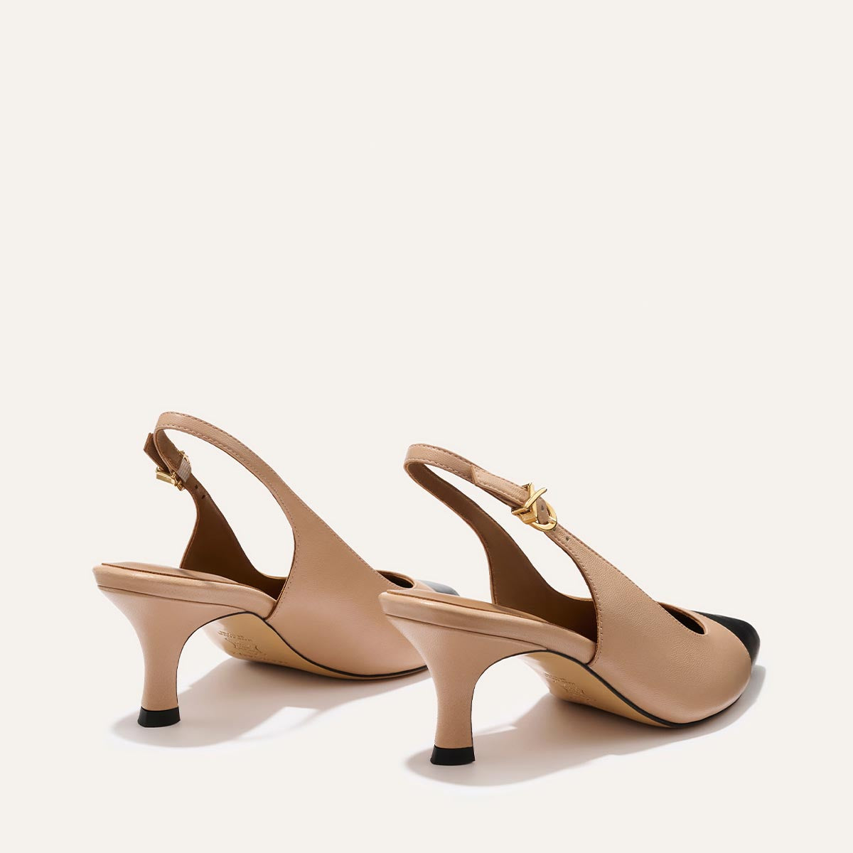 The Colette - Dune and Black Nappa by Margaux, beige slingback heels with black snip toe caps and gold buckle straps, are shown on a plain light background, angled away from view.