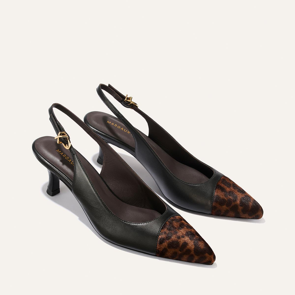 A pair of The Colette heels by Margaux in black nappa and leopard haircalf, featuring a snip nose design, a brown leopard print toe cap, and a gold buckle on the strap.