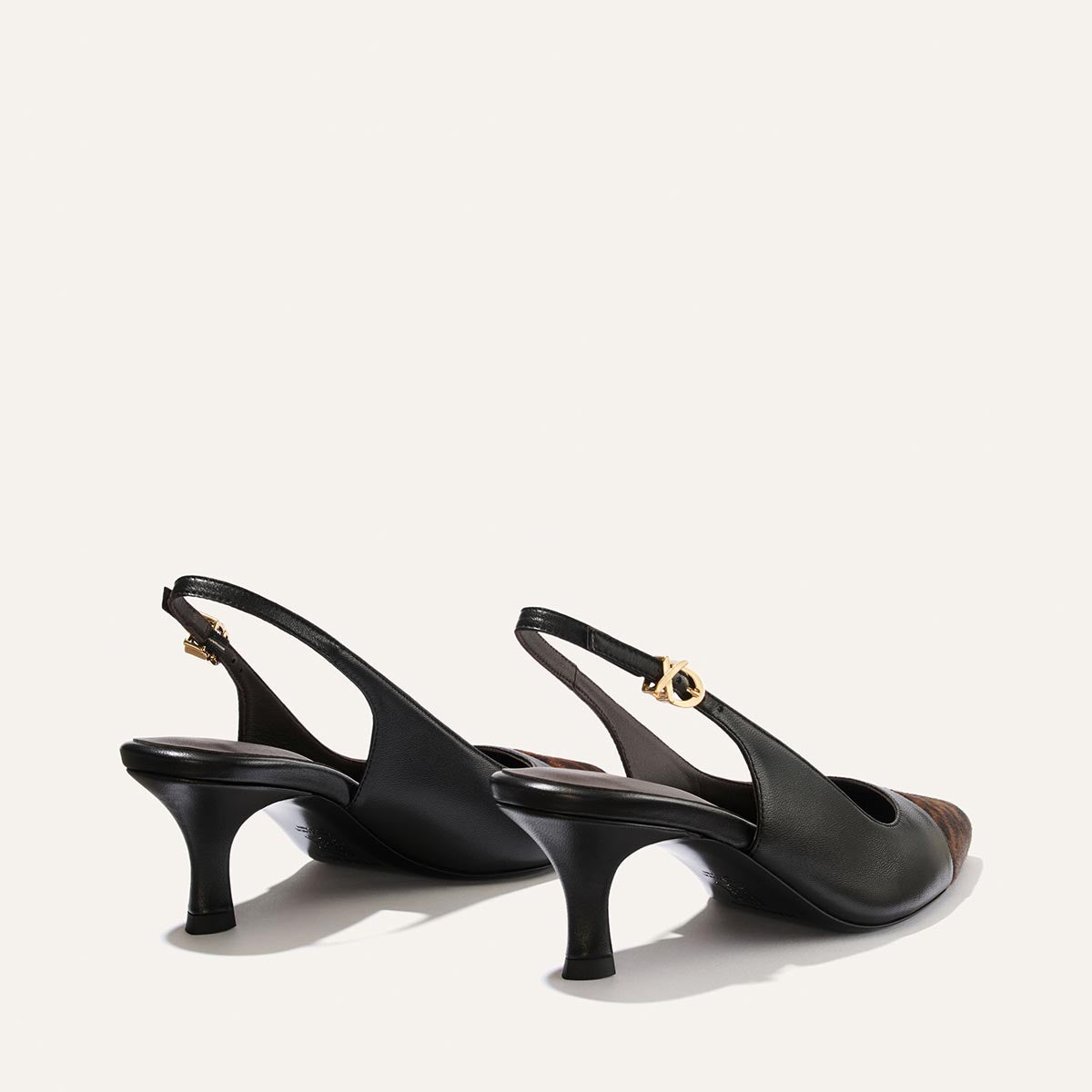 A pair of The Colette by Margaux in Black Nappa and Leopard Haircalf, featuring a chic snip toe and gold buckle accents, displayed from the back and side on a light background.