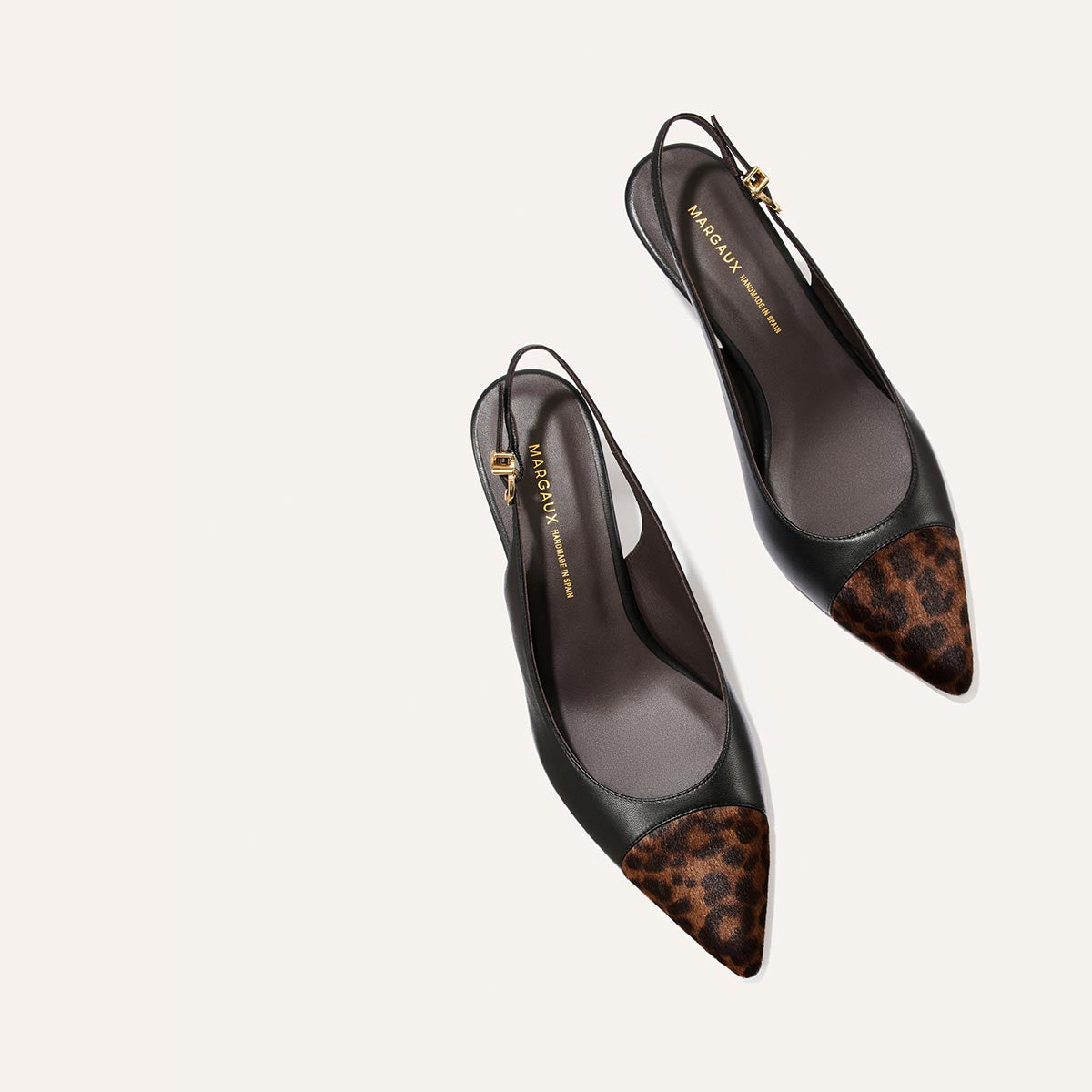 The Colette by Margaux—black nappa slingback flats with snip nose pointed toes and brown leopard haircalf detailing at the front, finished with a subtle micro heel—displayed on a light beige background.