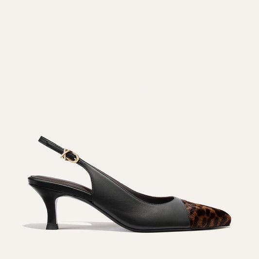 Margaux’s The Colette in Black Nappa and Leopard Haircalf is a black slingback heel with a micro heel and snip nose, featuring a leopard print front, leather upper, and a gold buckle on the ankle strap, set against an off-white background.