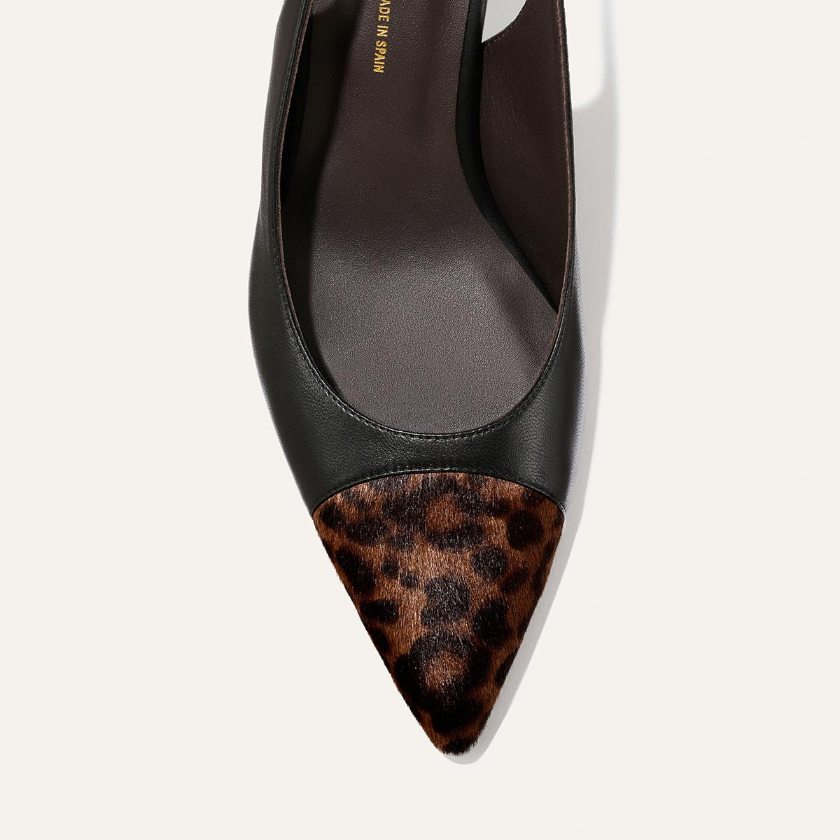A close-up of Margaux’s The Colette flat in Black Nappa and Leopard Haircalf, featuring a pointed toe, black leather body, brown and black leopard print haircalf toe cap, and a subtle micro heel, photographed against a plain white background.