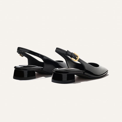 The Darcy Slingback by Margaux features black patent leather, low block heels, pointed toes, and gold buckle straps—ideal for warm-weather style—shown on a light background.
