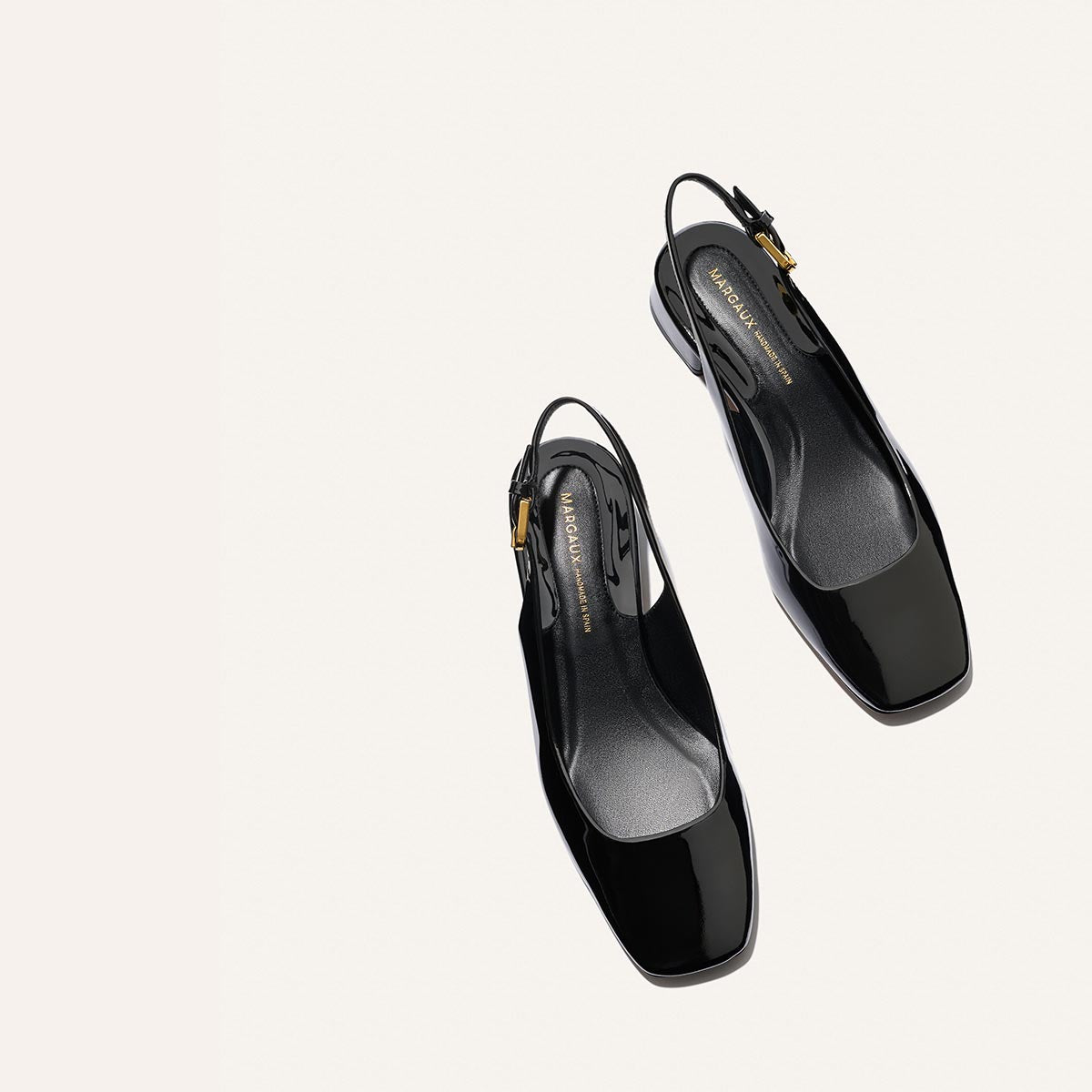 The Darcy Slingback - Black Patent by Margaux: sleek black patent leather ballet pumps with square toes and low heels, styled on a light beige background—ideal for chic, warm-weather looks.
