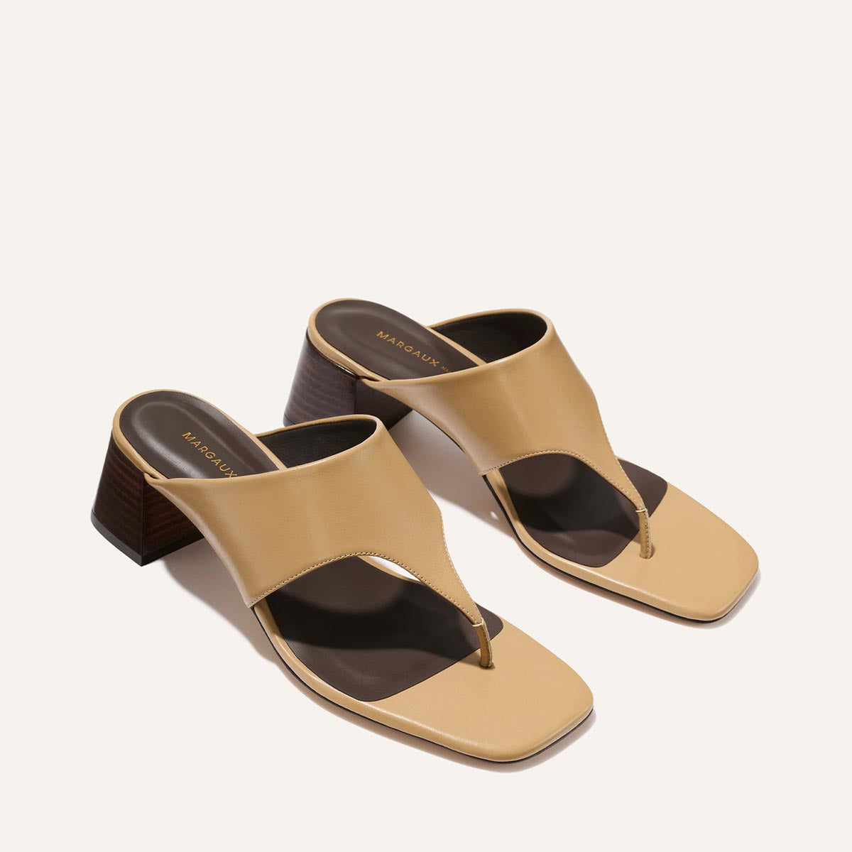 The Margaux Deia 50 - Praline Nappa is a pair of beige heeled sandals with wide straps, square toes, and dark brown block heels, shown on a light background.