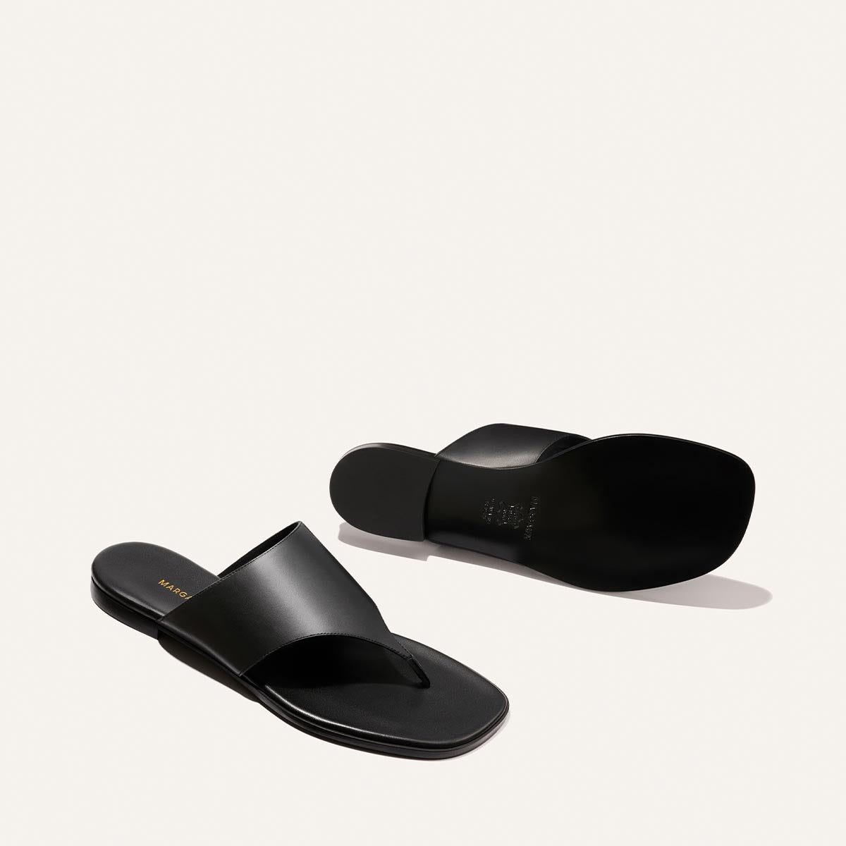 The Deia - Black Nappa by Margaux: a pair of black leather thong sandals with wide straps, one facing up and one down, displayed on a plain white background.