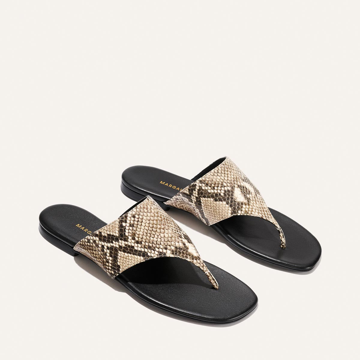 Pair of snake print sandals with black soles on a white background