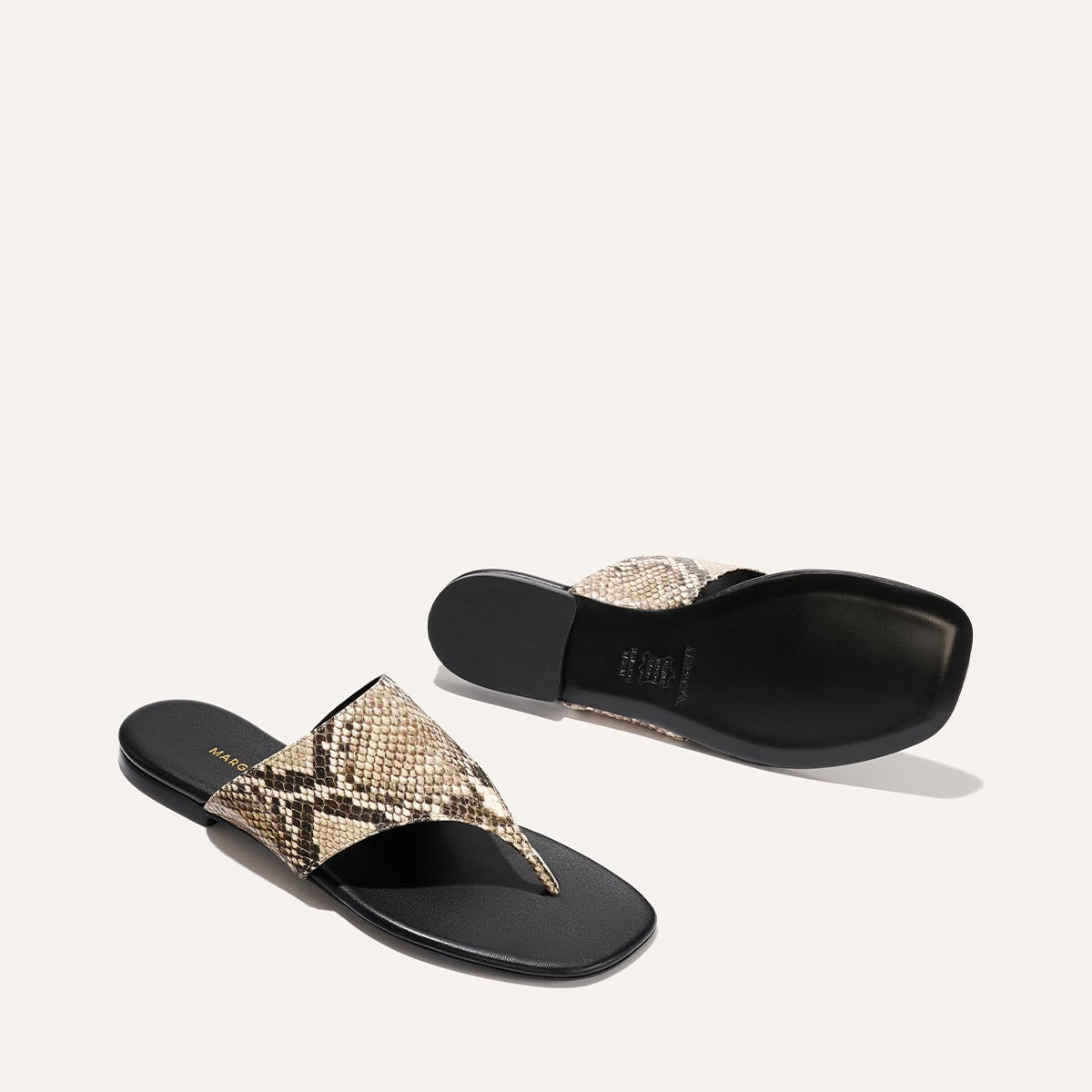 Pair of snake print sandals with black soles on a light gray background