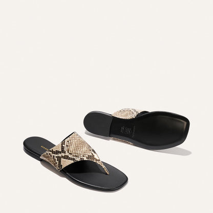 Pair of snake print sandals with black soles on a light gray background