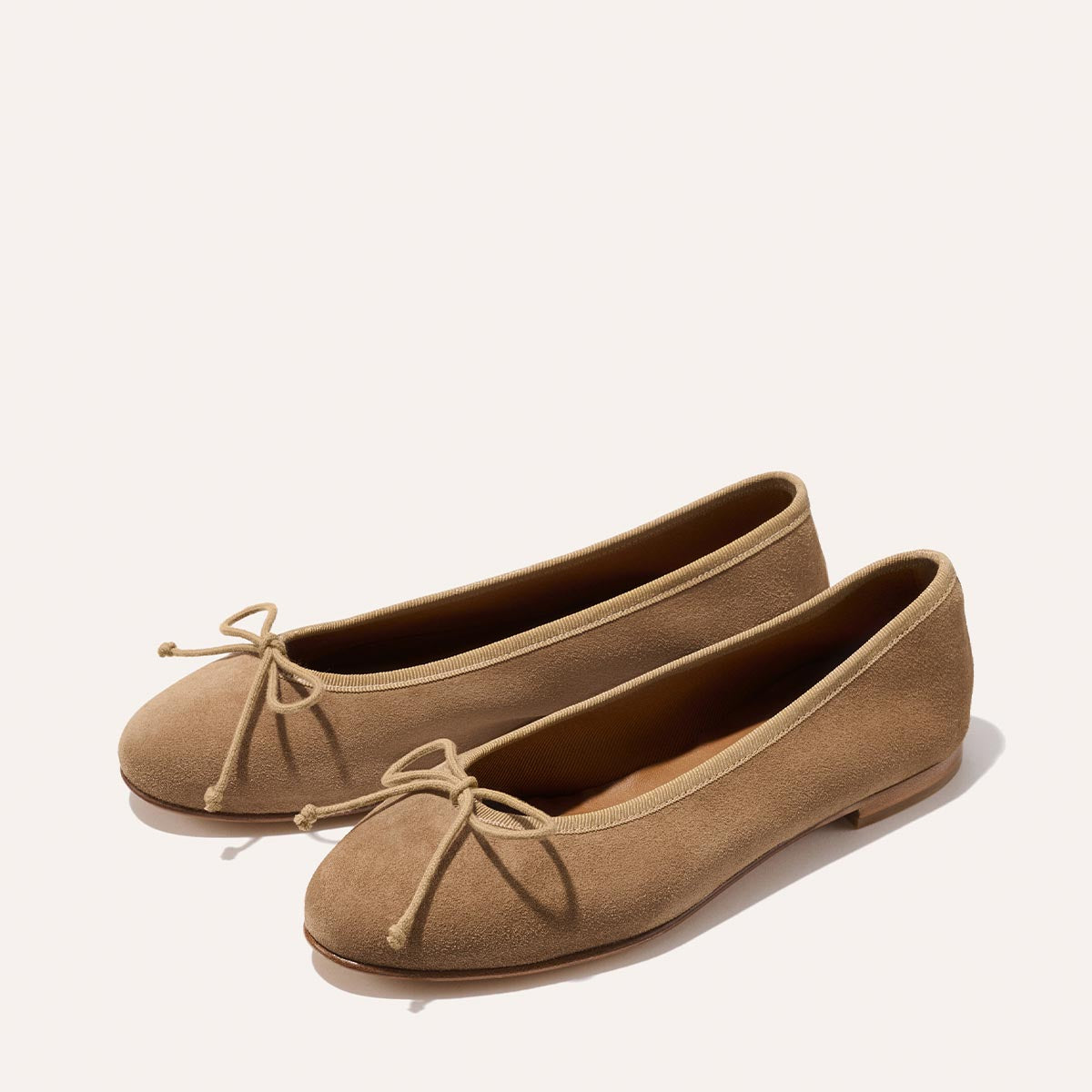 The Demi - Biscotti Suede by Margaux: handmade tan suede ballet flats with small bows, crafted in Spain and shown on a light background.