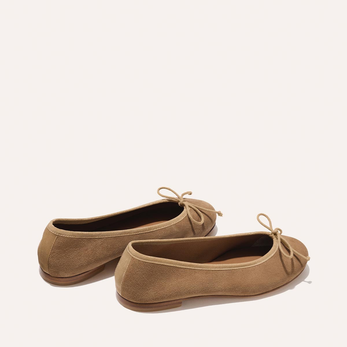 The Demi - Biscotti Suede by Margaux: Tan suede ballet flats with front bows, shown from back and side against a plain light background.