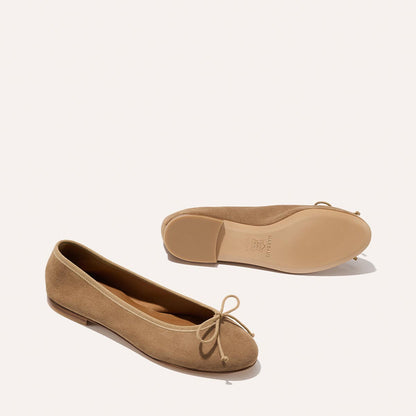 The Demi - Biscotti Suede by Margaux: comfortable tan suede ballet flats with small front bows, handmade in Spain. Shown on a light background; one shoe stands upright, the other lies on its side to show the sole.