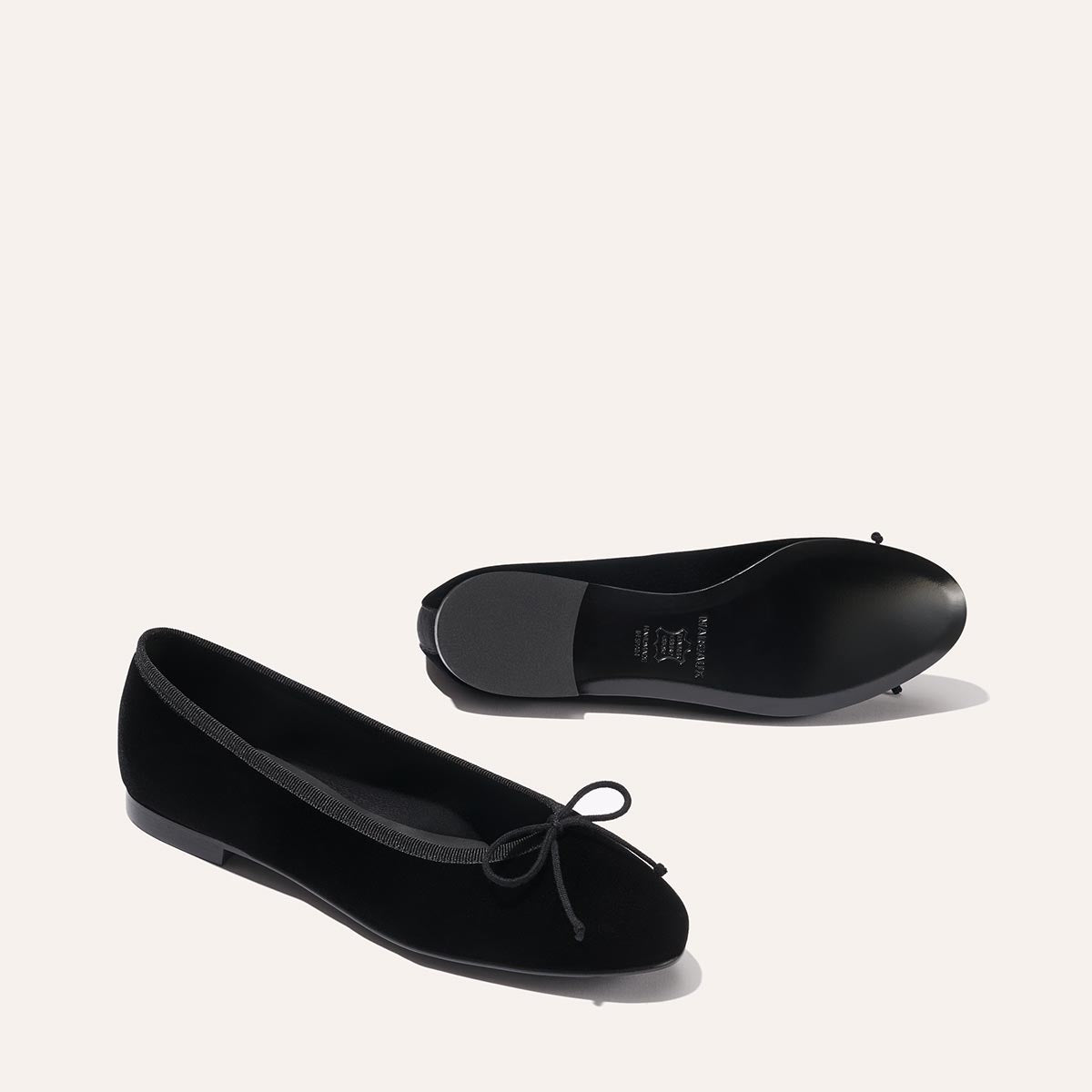 The Demi - Black Velvet by margaux-development: Black velvet ballet flats with a small bow detail. One shoe shows the top and side view, while the other reveals the sole, both placed on a plain, light background.
