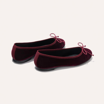 The Demi - Burgundy Velvet by margaux-development: a pair of burgundy velvet ballet flats with small matching bows, shown from the back and side on a plain light background.