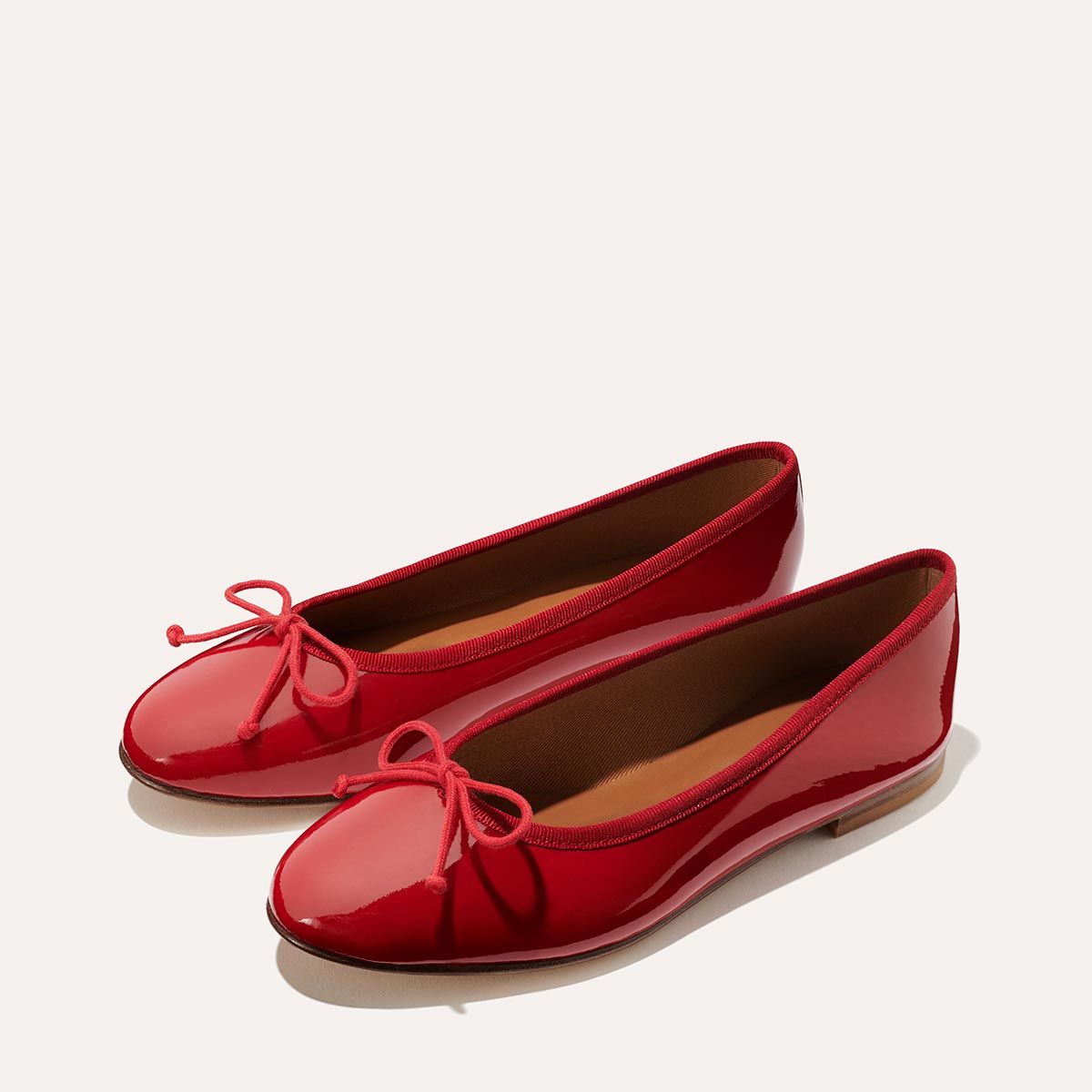 The Demi in Cherry Patent, a comfortable ballet flat with a rounded toe and adjustable cord bow detail.