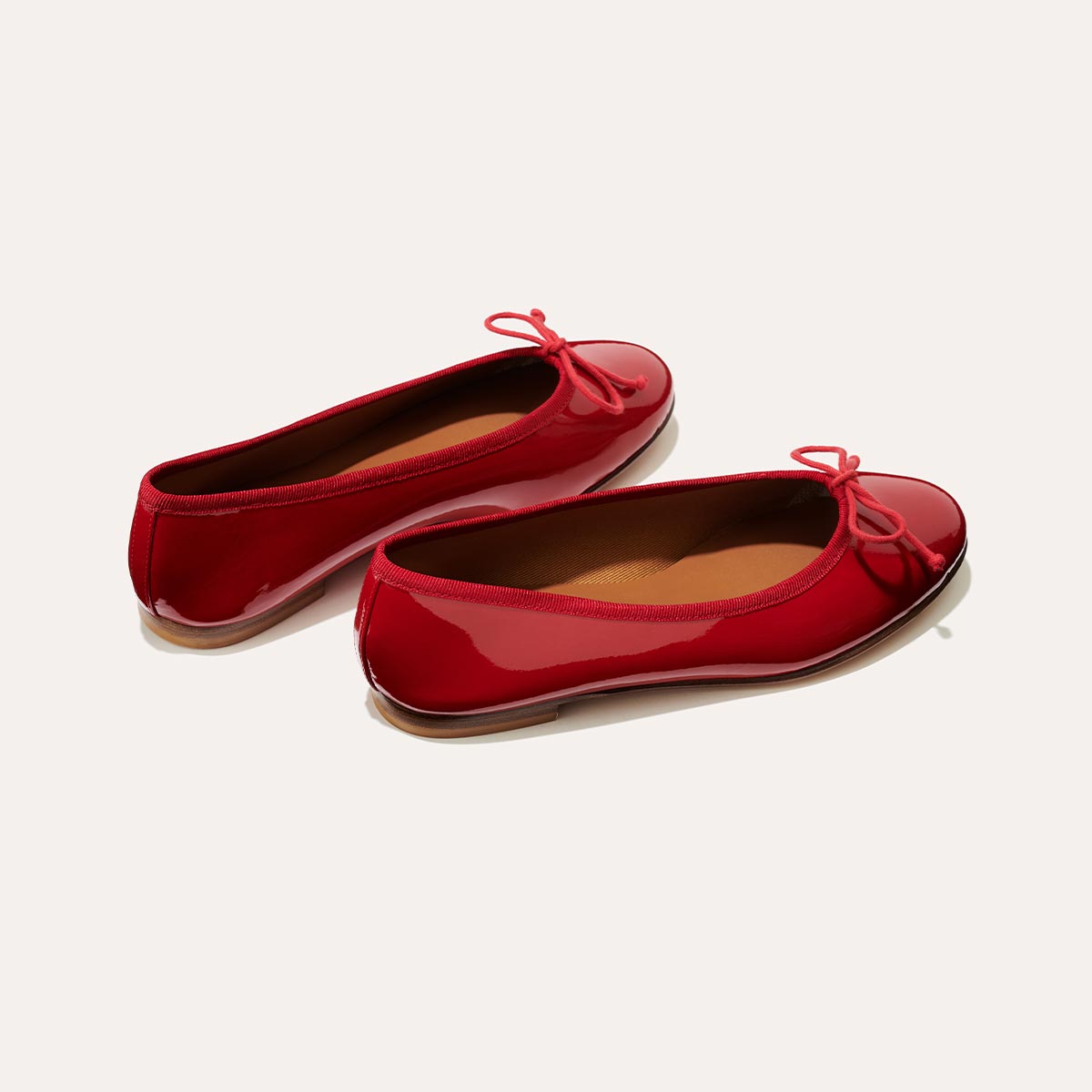 The Demi in Cherry Patent, a comfortable ballet flat with a rounded toe and adjustable cord bow detail.